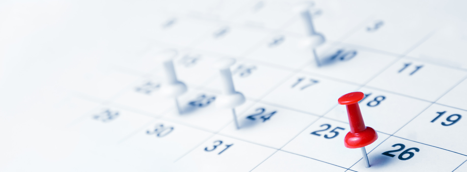 The image features a close-up view of a calendar with dates marked and a red push pin inserted into the 26th day, suggesting an event or reminder scheduled for that date.